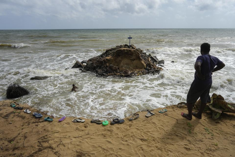 A man watches Nuwan Fernando, left, in the water, who wades in the tide to collect stones washed out from his land due to coastal erosion in Iranawila, Sri Lanka, Monday, June 19, 2023. "I don't know what will happen in the future but I still keep my faith," Fernando said, one of a few in Iranawila whose house remains intact. (AP Photo/Eranga Jayawardena)