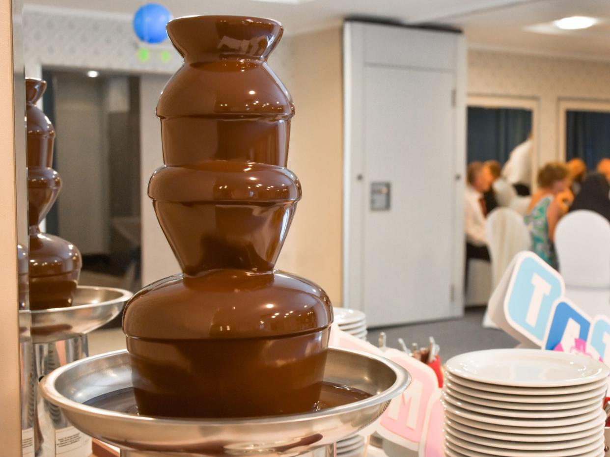 A chocolate fountain takes center stage on a restaurant's buffet table with other desserts. The sweet spread creates a festive atmosphere of culinary delight and luxury.