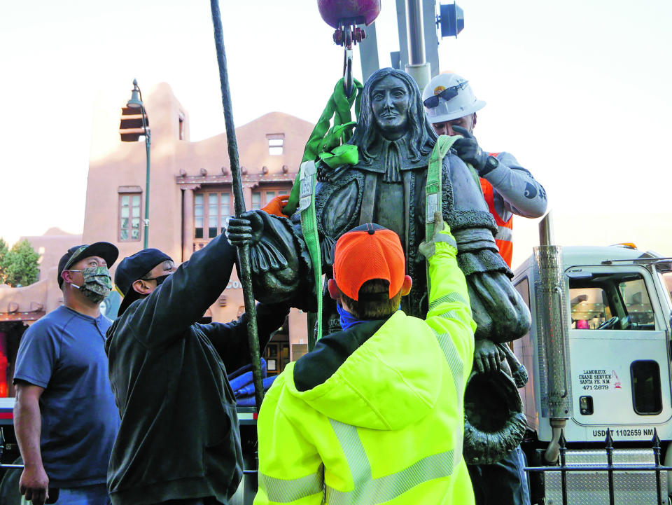 Workers fit straps to lift a statue of Spanish territorial governor Don Diego de Vargas from Cathedral Park on Thursday morning, June 18, 2020, in Santa Fe, N.M. Two other markers in the city were slated to come down as monuments to historical figures were being dismantled across the country. (Matt Dahlseid/Santa Fe New Mexican via AP)