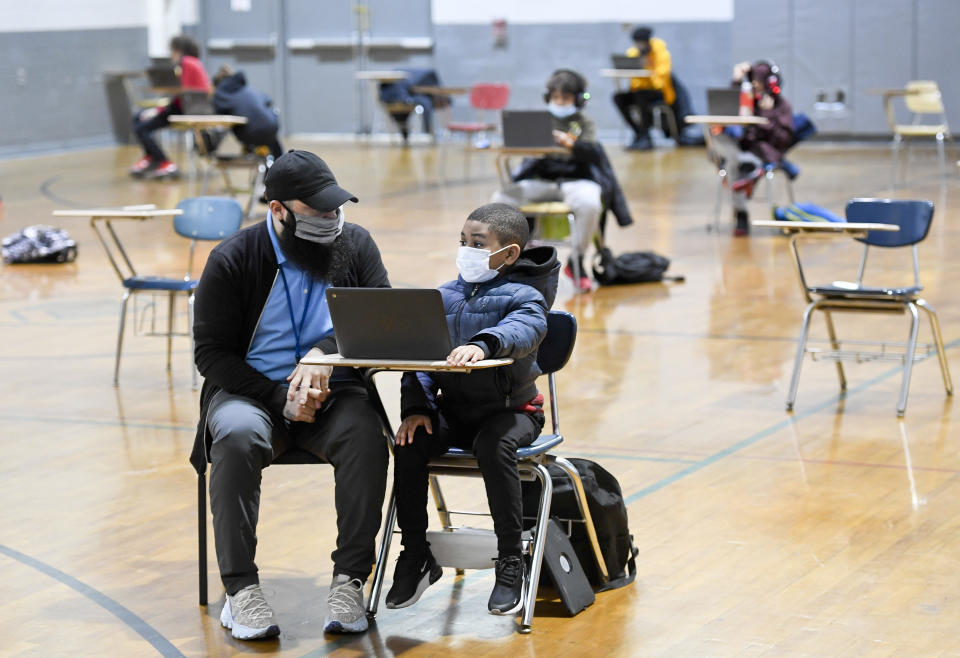 Reading, PA - January 19: Jordan Rodriguez, director of the Mulberry Street club, works with Santana Sanford, 7, a second grade student, as he does his school work on a laptop computer. At the Mulberry Street location of the Olivet Boys and Girls Club in Reading Tuesday morning January 19, 2021 where the club has resumed providing a location for students to come and do their remote learning with desks setup and spaced apart in the club's gym. The Reading School District has gone to all-virtual education as a precaution during the COVID-19 / Coronavirus Pandemic. (Photo by Ben Hasty/MediaNews Group/Reading Eagle via Getty Images)