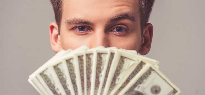 A man holding dollar bills up under his eyes