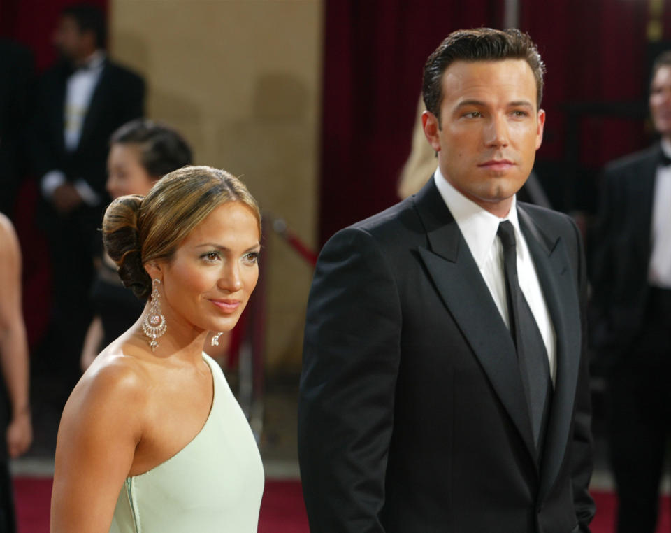 Jennifer Lopez in a strapless gown stands beside Ben Affleck in a black suit on the red carpet