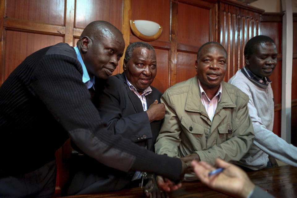 Kenya Police officer puts handcuffs onto Francis Kinyili, left, Stephen Soi, centre, and Richard Ekai, right, after they were charged with corruption at Milimani Court, in Nairobi, Kenya, Monday, Oct. 15, 2018. The three men face six counts of abuse of office and four counts of wilful failure to comply with the law relating to the management of public funds. (AP Photo/Brian Inganga)