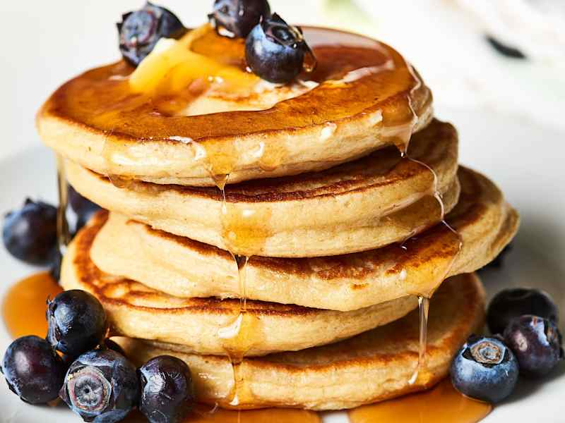 Stacks of pancakes, drizzled with syrup and garnished with blueberries, on a plate