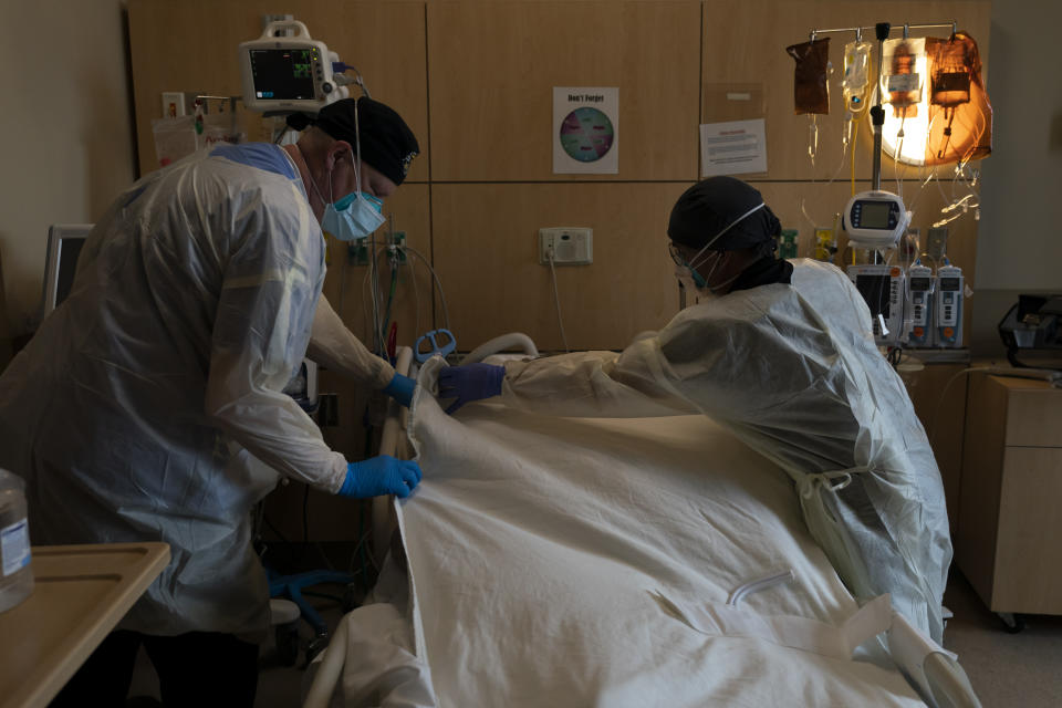 FILE - Respiratory therapist Frans Oudenaar, left, and registered nurse Bryan Hofilena cover a body of a COVID-19 patient with a sheet at Providence Holy Cross Medical Center in Los Angeles, Tuesday, Dec. 14, 2021. On Thursday, May 12, 2022, Gov. Gavin Newsom's administration proposed sending $1,000 checks to workers in hospitals and nursing homes in recognition of their dangerous work during the pandemic. The money would go to anyone who works inside a hospital or a nursing home-including doctors, nurses and other support staff.(AP Photo/Jae C. Hong, File)