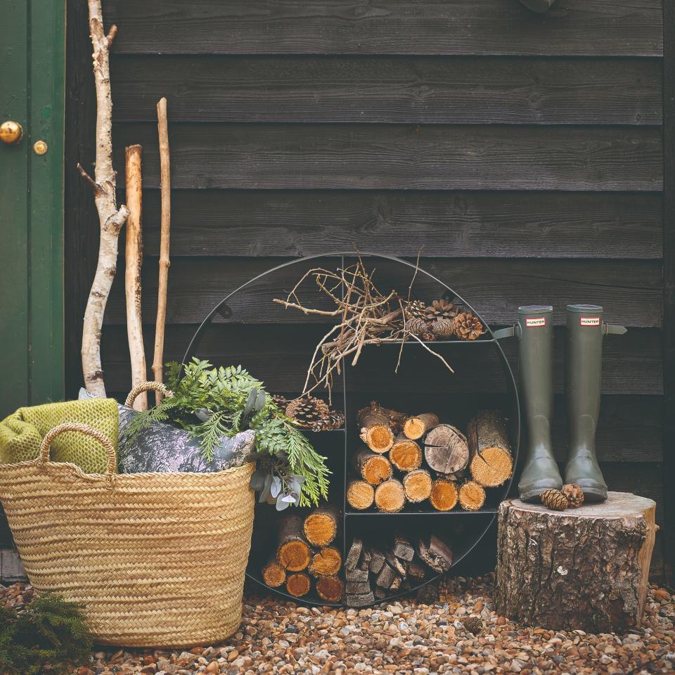 A pile of wood next to wellington boots and a basket with blankets