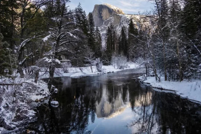 A dusting of snow covers the trees and Half Dome seen in the distance in Yosemite Valley