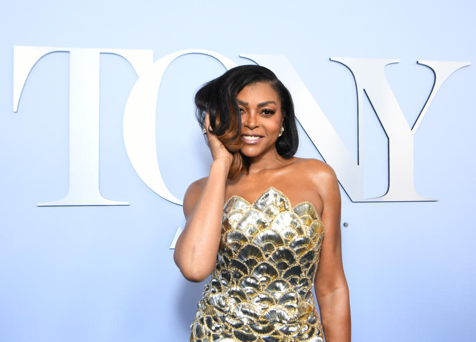 Taraji P. Henson poses in front of "TONY" sign in a strapless, sequined gown with a scallop pattern. She smiles with one hand touching her hair