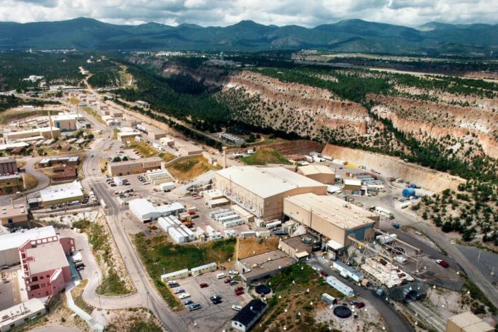 Une vue aérienne des bâtiments et des voitures à côté des montagnes boisées à l'horizon.