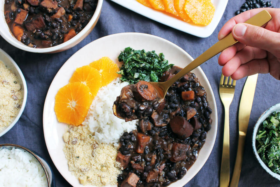 Table set with various plates, including a main plate containing vegan Feijoada, also known as Brazilian black bean stew.