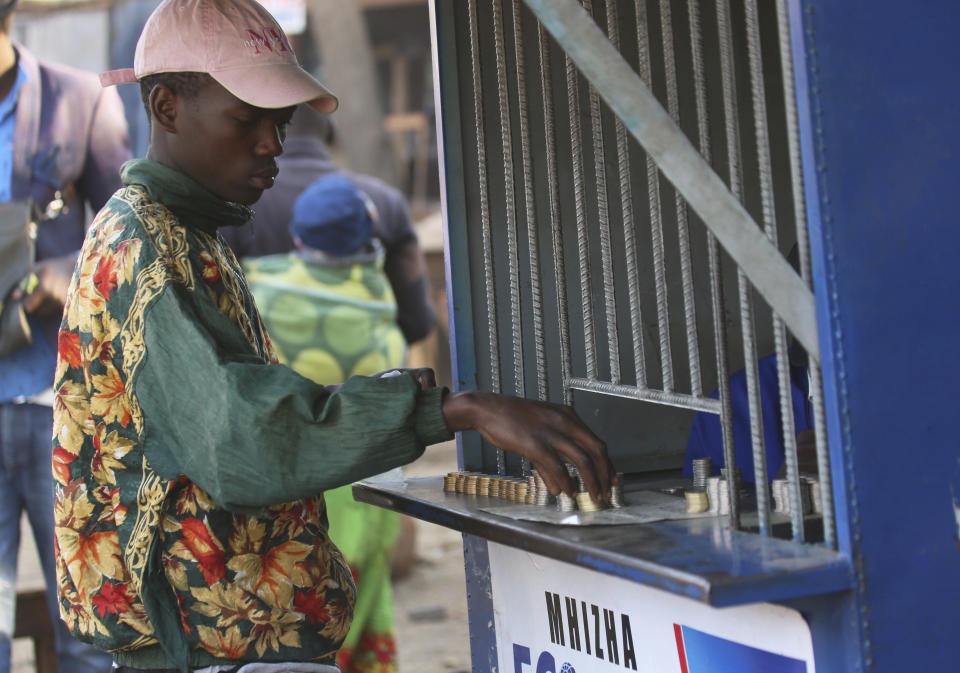 In this photo taken Thursday, Aug. 8, 2019, a client collects coins he bought from a vendor at a premium in Harare, Zimbabwe. With inflation soaring and cash in short supply, many Zimbabweans transfer funds using their mobile phones and pay a premium to get currency. (AP Photo/Tsvangirayi Mukwazhi)