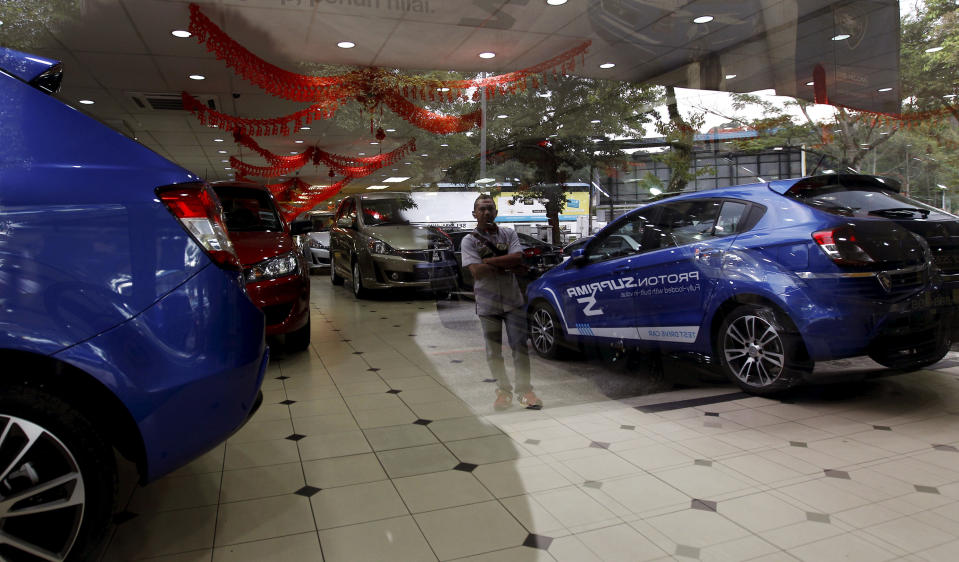 A man looking at a new car displayed outside is reflected on a car showroom glass in Kuala Lumpur, Malaysia, Monday, Jan. 20, 2014. Malaysia's government unveiled Monday a new auto policy, offering incentives and easing curbs on the production of small, energy-efficient cars as it vies for investment with neighboring rivals Thailand and Indonesia. (AP Photo/Daniel Chan)