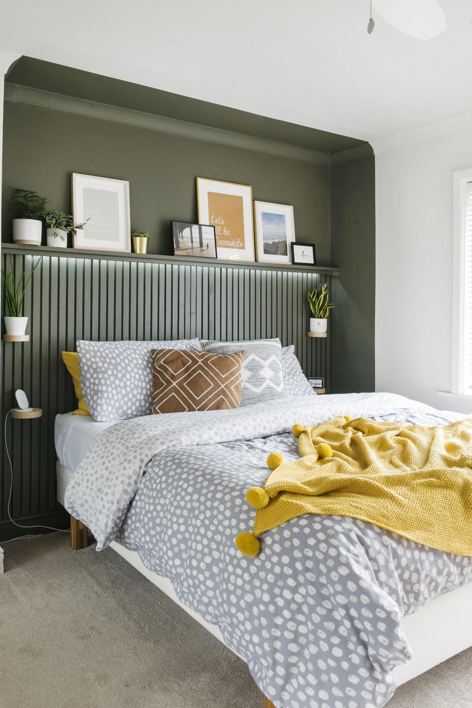 Bedroom with bed in alcove painted in dark green tone, with slim slatted panelling up to picture rail height and a shelf with artwork on above