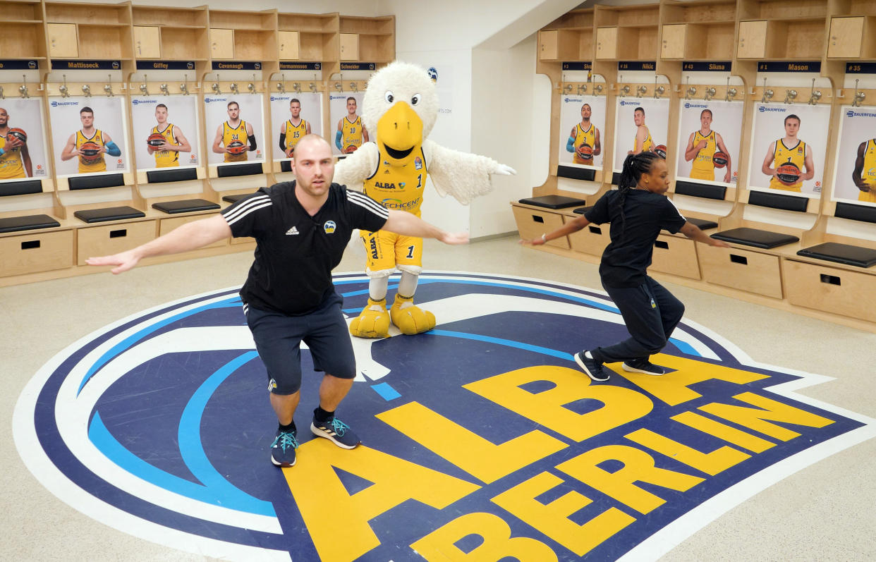 Das Standbild aus einem Video zeigt die beiden Trainer Stefan Ludwig und Elisa Lierhaus mit Maskottchen Albatros bei ALBAs tägliche Sportstunde in der Umkleidekabine des Basketball-Bunsdesligisten ALBA BERLIN. Foto: ALBA BERLIN/dpa 