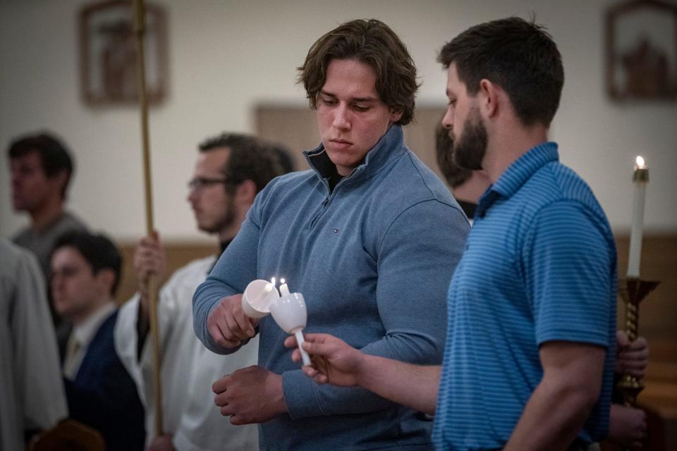 Charles Wesley, 21, of Clinton Township, left, and Joe Muzljakovich, 23, of Traverse City, are participating in the Order of Christian Initiation for Adults to be fully realized members of the Catholic faith as they light candles before entering St. Joseph Hall for the Transfer of the Most Blessed Sacrament Thursday, April, 6, 2023, at Our Lady of the Rosary Catholic Church in Detroit.