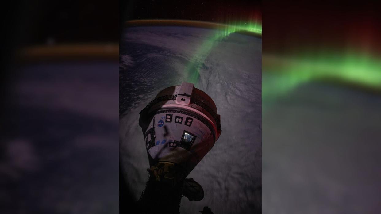  A cone-shaped spacecraft in front of a green aurora above the earth, which is in shadow. 