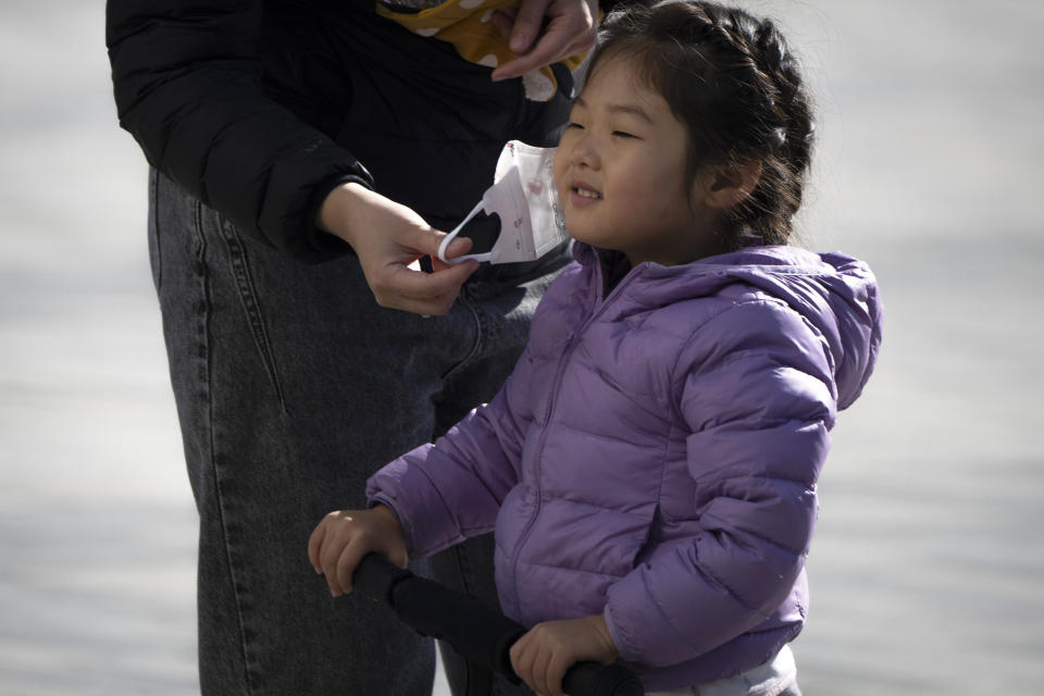 A woman removes a girl's face mask as she plays on a plaza in Beijing, Saturday, Nov. 5, 2022. (AP Photo/Mark Schiefelbein)