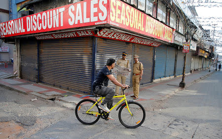 A man pedals his bicycle past police officers standing in front of the closed shops during a strike called by Bharatiya Janata Party (BJP) and Rashtriya Swayamsevak Sangh (RSS) to protest against state government for allowing two women to defy an ancient ban and enter the Sabarimala temple, in Kochi, January 3, 2019. REUTERS/Sivaram V