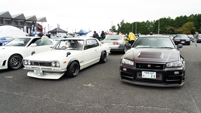 in an outdoor parking lot, a white 1970s skyline gt-r parked next to a 1990s r34 gt-r