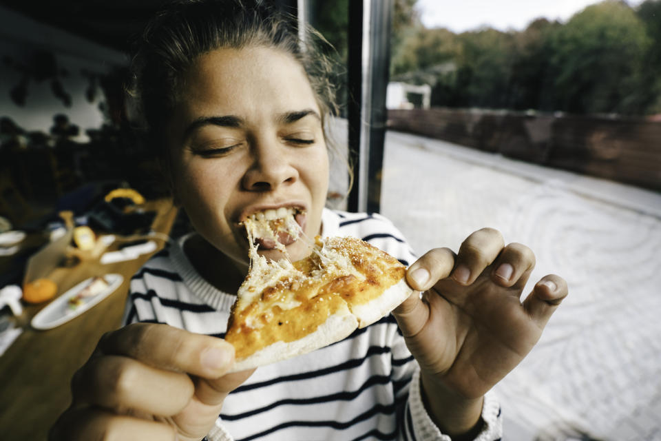 A person with a striped sweater enjoys a slice of pizza at an outdoor table