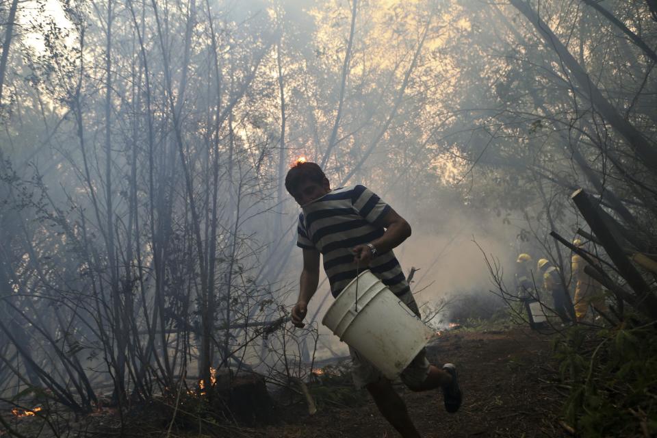In this Saturday, Jan. 28, 2017 photo, a resident helping firefighters runs with an empty water bucket as they fight wildfires in Paso El Leon, in Concepcion, Chile. Residents of some communities have been battling the fires themselves, without any protective gear and often using just branches or bottles of water in a frantic effort to save their homes, pasture and livestock. (AP Photo/Esteban Felix)