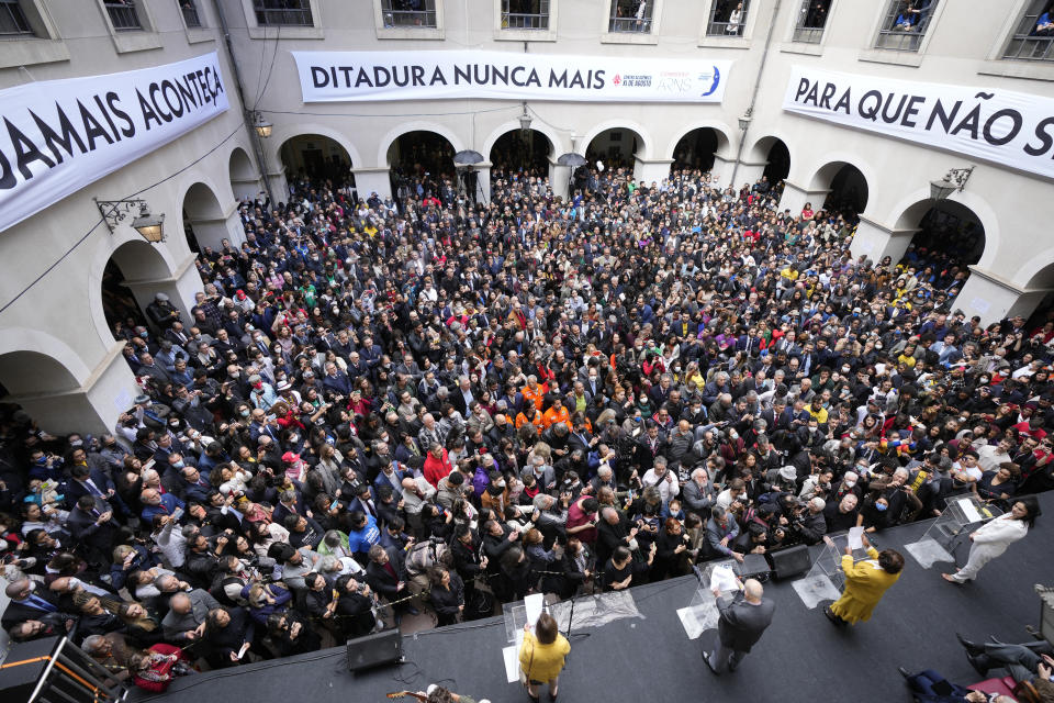 People attend the reading of one of two manifestos defending the nation's democratic institutions and electronic voting system outside the Faculty of Law at Sao Paulo University in Sao Paulo, Brazil, Thursday, Aug. 11, 2022. The two documents are inspired by the original "Letter to the Brazilians" from 1977 denouncing the brutal military dictatorship and calling for a prompt return of the rule of law. The sign reads in Portuguese "Dictator never again." (AP Photo/Andre Penner)