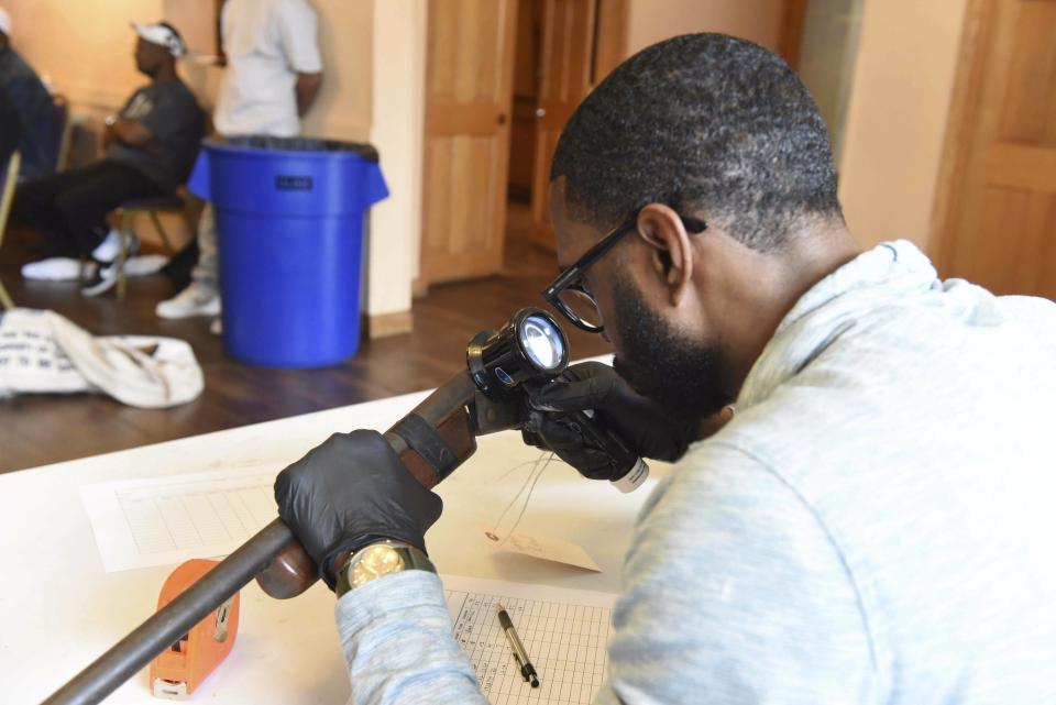 In this June 2, 2018 photo provided by the Chicago Police Department, a forensic firearms examiner inspects a weapon turned in during a gun buy-back program in the 6th Police District on the South Side. Officers in the district have recovered more than 1,200 firearms this year. (CPD via AP)