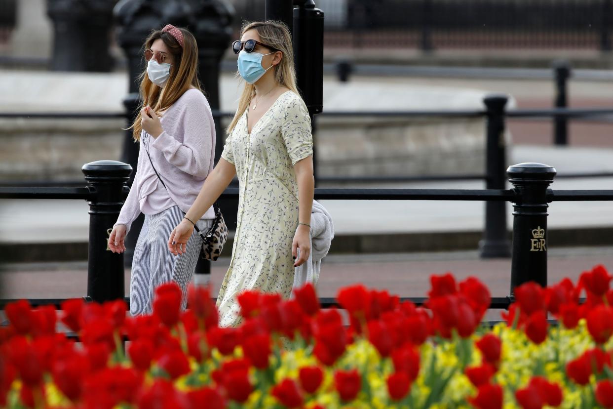 Two women wear protective face masks as they walk past the flowers outside Buckingham Palace in London on April 12, 2020, during the nationwide lockdown to combat the novel coronavirus pandemic. - The Prime Minister left hospital on Sunday to convalesce from coronavirus at Chequers, the country estate of British prime ministers, officials said, a week after he was admitted and then spent three days in intensive care. (Photo by Tolga AKMEN / AFP) (Photo by TOLGA AKMEN/AFP via Getty Images)