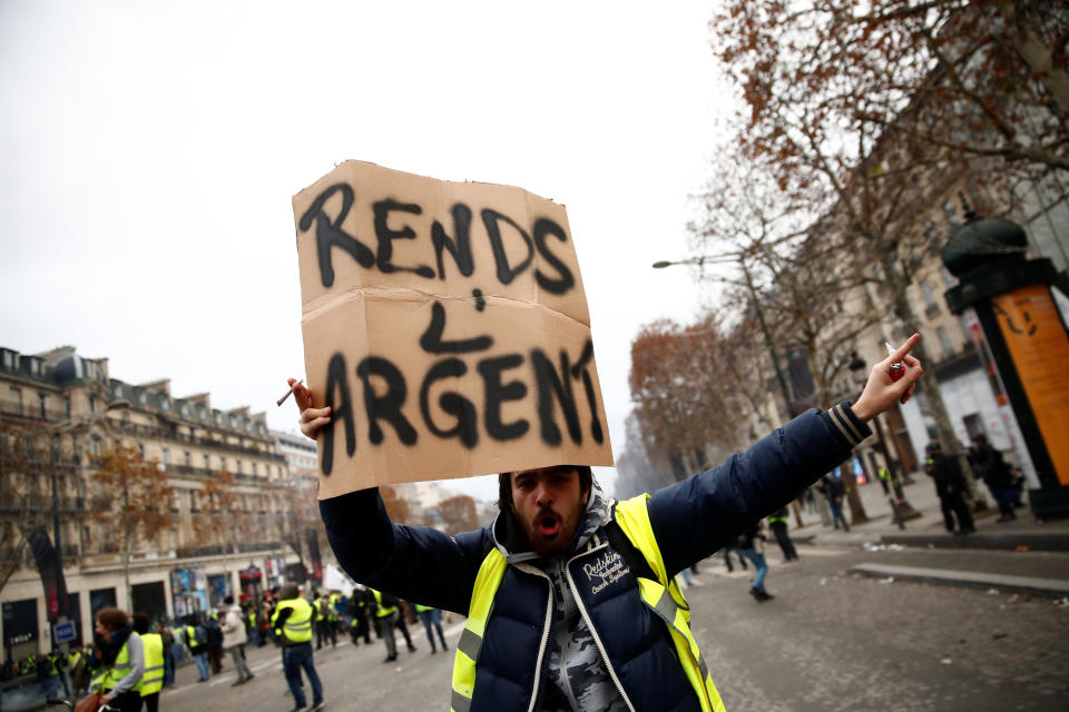 A protester wearing a yellow vest holds a placard reading “Give back money” on the Champs-Elysees Avenue during a national day of protest by the “yellow vests” movement in Paris, France, Dec. 8, 2018. (Photo: Christian Hartmann/Reuters)