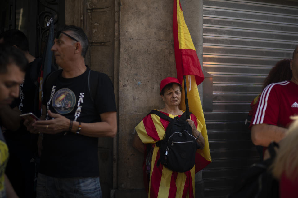 A woman holding a Spanish flag stands on the sidewalk as members of National Police and Guardia Civil protest demanding better pay in Barcelona, Spain, Saturday, Sept. 29, 2018. (AP Photo/Felipe Dana)