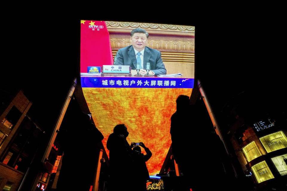 People wearing face masks to help curb the spread of the coronavirus gather near a giant TV screen broadcasting a news of Chinese President Xi Jinping speaks as he participates in a virtual G20 summit, at a shopping mall in Beijing, Sunday, Nov. 22, 2020. The Group of 20 summit opened on Saturday with appeals by the world's most powerful leaders to collectively chart a way forward as the coronavirus pandemic overshadows this year's gathering, transforming it from in-person meetings to a virtual gathering of speeches and declarations. (AP Photo/Andy Wong)