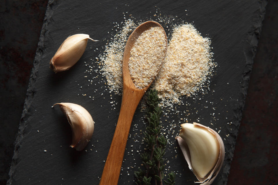 Close up composition of garlic powder sprinkled into wooden spoon, two sprigs of thyme and three cloves on black slate board. Selective focus (geemly / Getty Images stock)