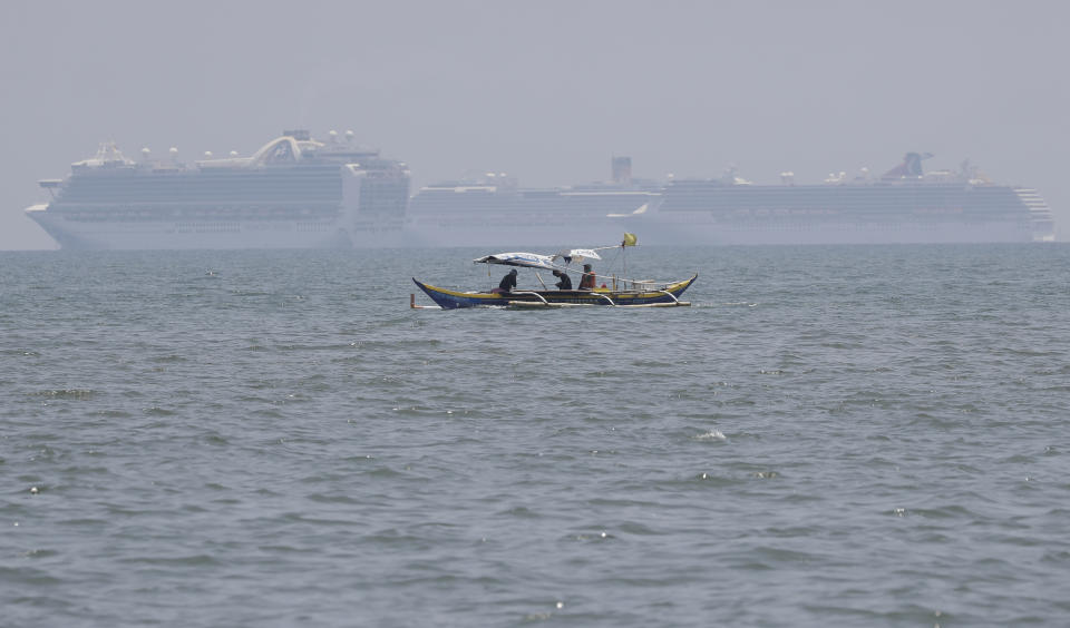 A fishing boat passes in front of the Ruby Princess cruise ship, left, and other ships as they are anchored in the Manila Bay, Philippines, Thursday, May 7, 2020. The Ruby Princess which is being investigated in Australia for sparking coronavirus infections, has sailed into Philippine waters to bring Filipino crewmen home. (AP Photo/Aaron Favila)