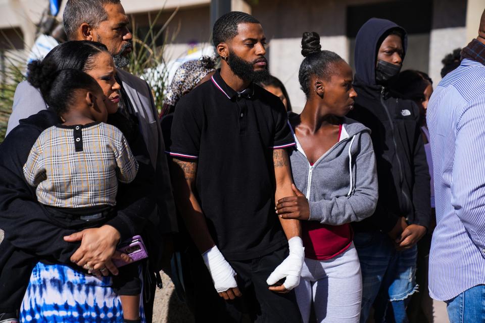 Javon Johnson, 25, center, listens as the Rev. Jarrett Maupin addresses the media during a news conference for Johnson and Taylor Thomas, 13, outside Phoenix police headquarters on Feb. 2, 2022, in downtown Phoenix. Both Johnson and Thomas were injured by Phoenix police officers on Jan. 31, 2022.