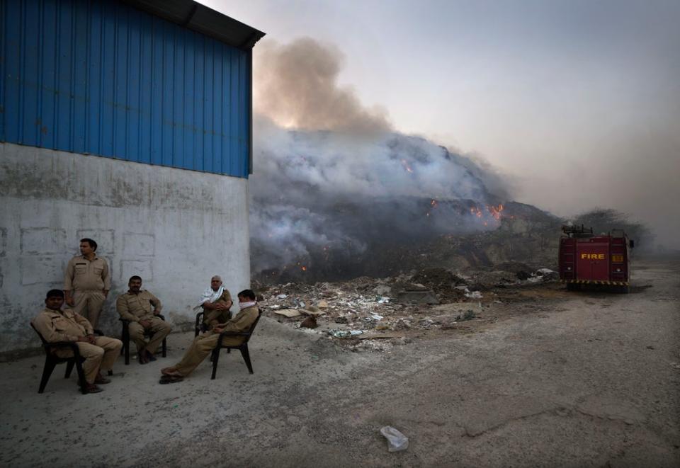 Delhi fire officials take a break while dousing a fire at the Bhalswa landfill in New Delhi on Wednesday. (AP)