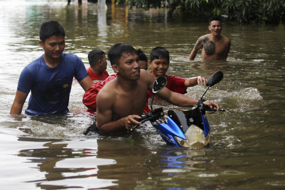 Residents push a motorbike at a flooded neighborhood in Makassar, South Sulawesi, Indonesia, Wednesday, Jan. 23, 2019. Torrential rains that overwhelmed a dam and caused landslides killed at least six people and displaced more than 2,000 in central Indonesia, officials said Wednesday. (AP Photo/Masyudi Syachban Firmansyah)