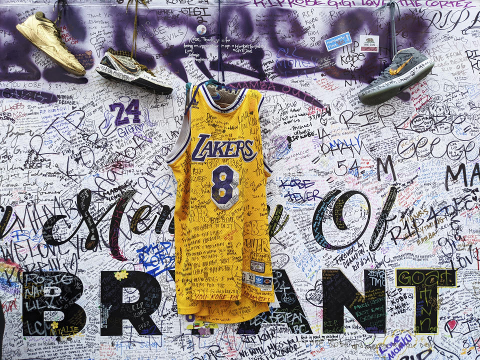 FILE - In this Feb. 2, 2020, file photo, sneakers and a Los Angeles Lakers uniform with the numbers worn by NBA star Kobe Bryant are left at a memorial for Bryant while fans gather to pay their respect near Staples Center in Los Angeles. Bryant, the 18-time NBA All-Star who won five championships and became one of the greatest basketball players of his generation during a 20-year career with the Lakers, died in a helicopter crash Sunday, Jan. 26. (AP Photo/Damian Dovarganes, File)