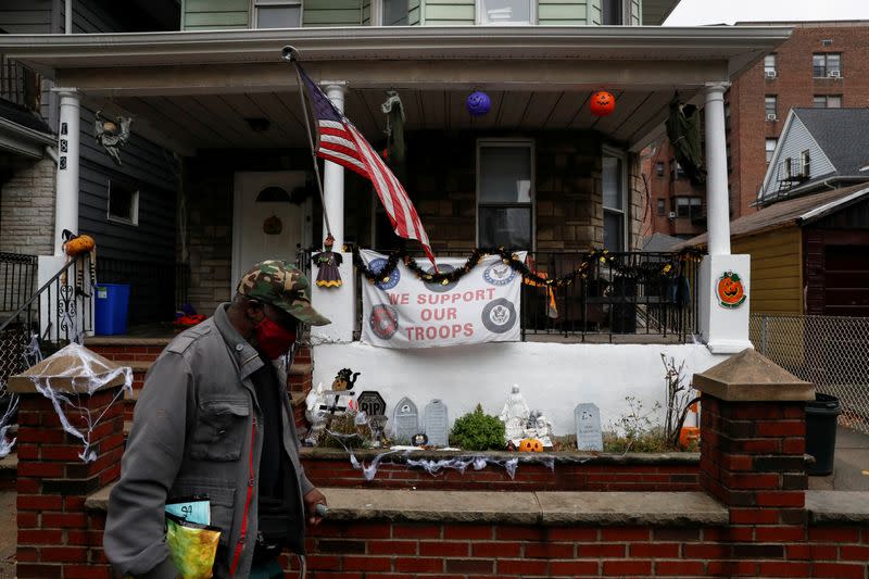 FILE PHOTO: A man wearing a protective face mask walks by the U.S. flag and Halloween decorations as the spread of coronavirus disease (COVID-19) continues in the borough of Brooklyn in New York