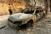 Tom Stokesberry with the U.S. Forest Service walks past a destroyed car after the Soberanes Fire burned through the Palo Colorado area, north of Big Sur, California, U.S. July 31, 2016. REUTERS/Michael Fiala