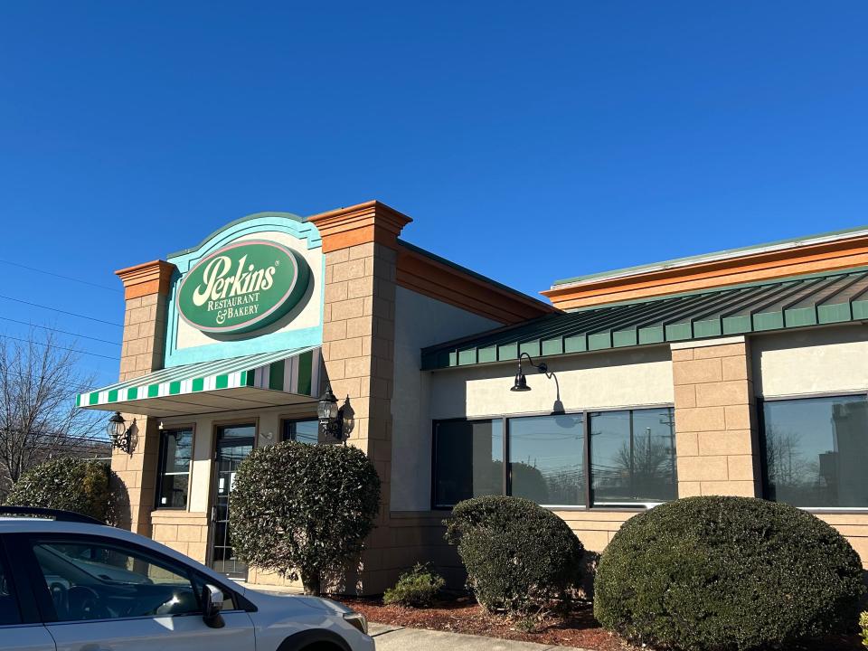 Exterior of Perkins with green roofing and green oval-shaped logo in front of a blue sky