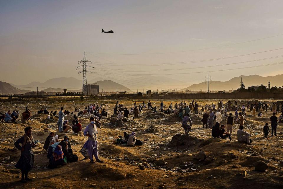 PHOTO: A military transport plane departs overhead as Afghans hoping to leave the country wait outside the Kabul airport on Aug. 23, 2021. (Marcus Yam/Los Angeles Times via Getty Images, FILE)