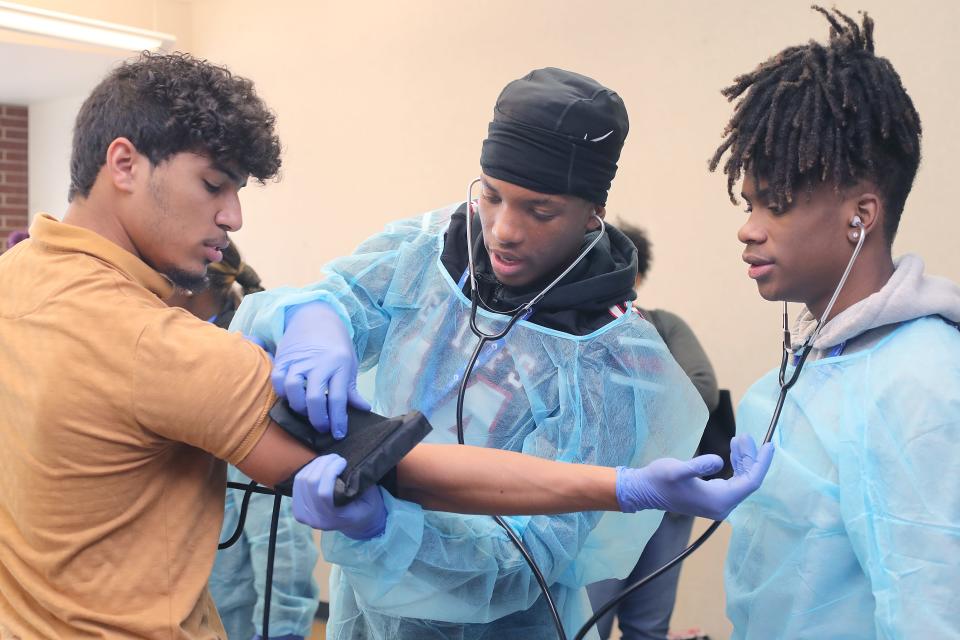 NEOMED student Luis Pozo, left, works with Buchtel High School students Damien Johnson and Diaire Pride on taking a blood pressure during a Black Men in White Coats Summit on Thursday, Oct. 27, 2022 in Akron, Ohio, at the University of Akron.