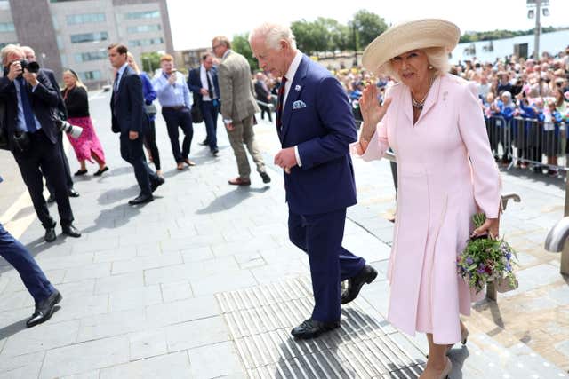 The Queen waves at the camera she walks next to the King