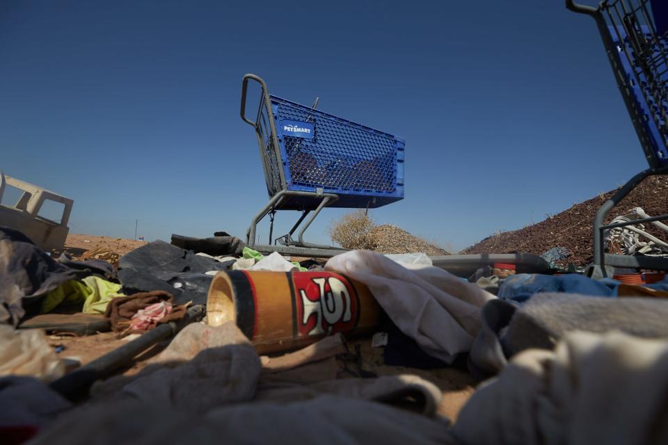 Carts, articles of clothing and other objects are scattered about in a space where many people experiencing homelessness gather in Goodyear on May 2, 2022.