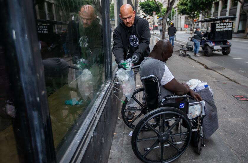 Los Angeles, CA June 1: Simon "Angel" Melendrez, left, with the Overdose Response Teams from Homeless Healthcare Los Angeles attempts to assist a man June 1, 2023, in Los Angeles, CA. He and his partner Aurora Morales, Overdose Response Team Lead, right, spotted a man slumped forward in his wheelchair, blood dripping from his brow. A woman passing told them he had been like that for hours. Melendrez shook the man's shoulder, slipped a pulse oximeter on his finger, and tried to coax him to take a deep breath before hoisting the oxygen tank to the sidewalk and they try and give him oxygen. The man pulls the oxygen mask off his face. (Francine Orr / Los Angeles Times)
