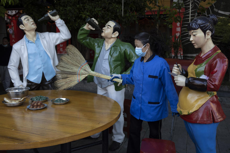 A cleaner wearing a mask to help stop the spread the coronavirus sweeps replicas of food and statues depicting normal life along a retail street in Wuhan, central China's Hubei province, Thursday, April 9, 2020. Released from their apartments after a 2 1/2-month quarantine, residents of the city where the coronavirus pandemic began are cautiously returning to shopping and strolling in the street but say they still go out little and keep children home while they wait for schools to reopen. (AP Photo/Ng Han Guan)