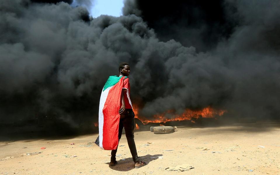 A person wearing a Sudan's flag stand in front of a burning pile of tyres during a protest against prospect of military rule in Khartoum, Sudan - REUTERS