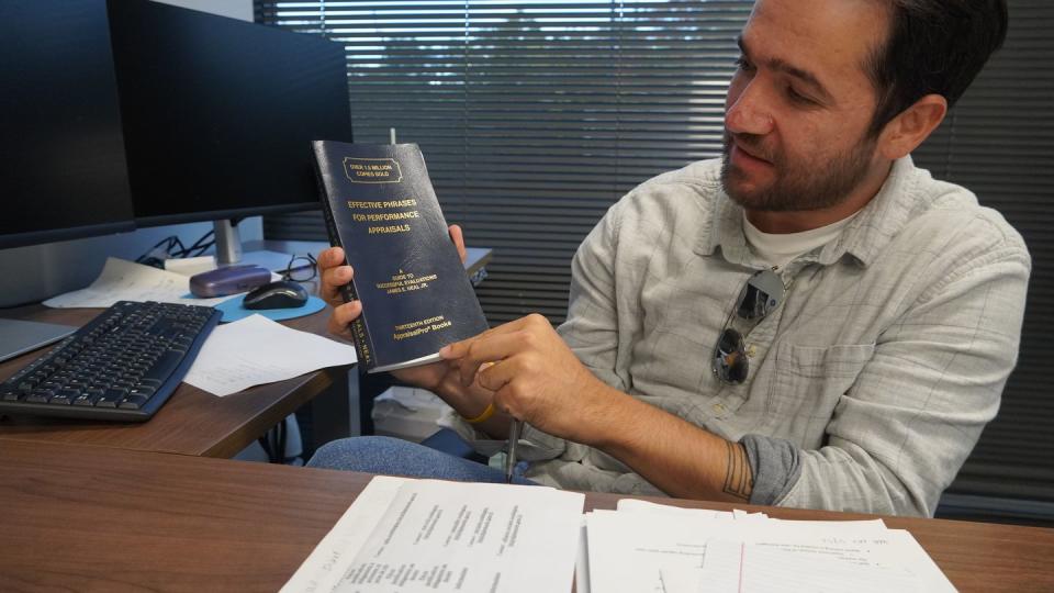 Satary, seated in his office, shows off his handbook for performance reviews. He oversees a team of thirty as the director of employment services for Lutheran Social Services National Capital Area. (Jaime Moore-Carrillo)