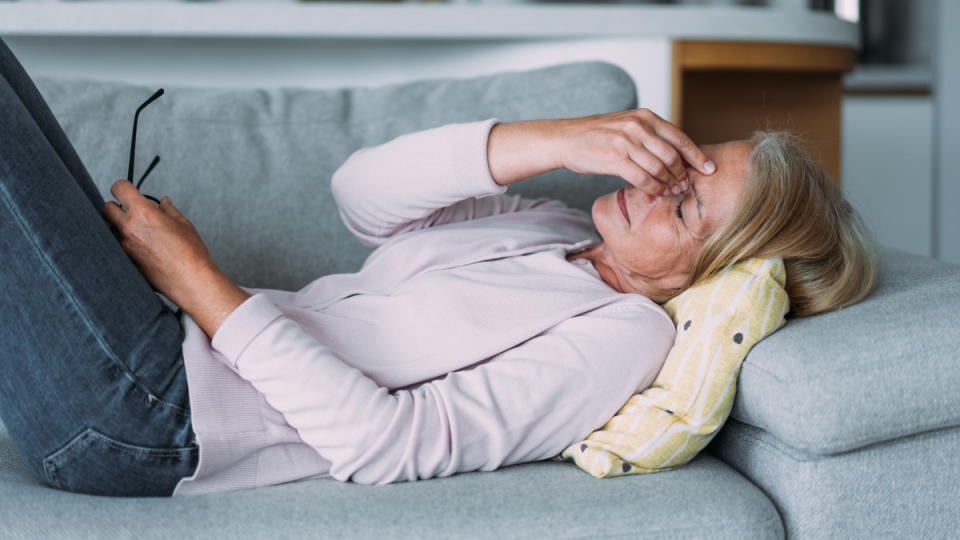 A woman falling asleep on the couch after eating, which can be a sign of diabetes, as she holds her hand to her face