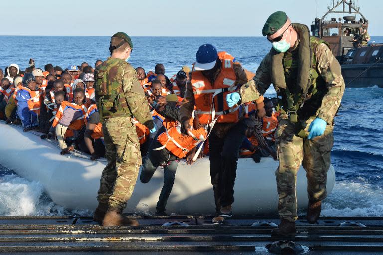 British Royal Marines help migrants disembark from an inflatable boat onto a landing craft of HMS Bulwark after being rescued around 40 miles off the coast of Libya on May 13, 2015